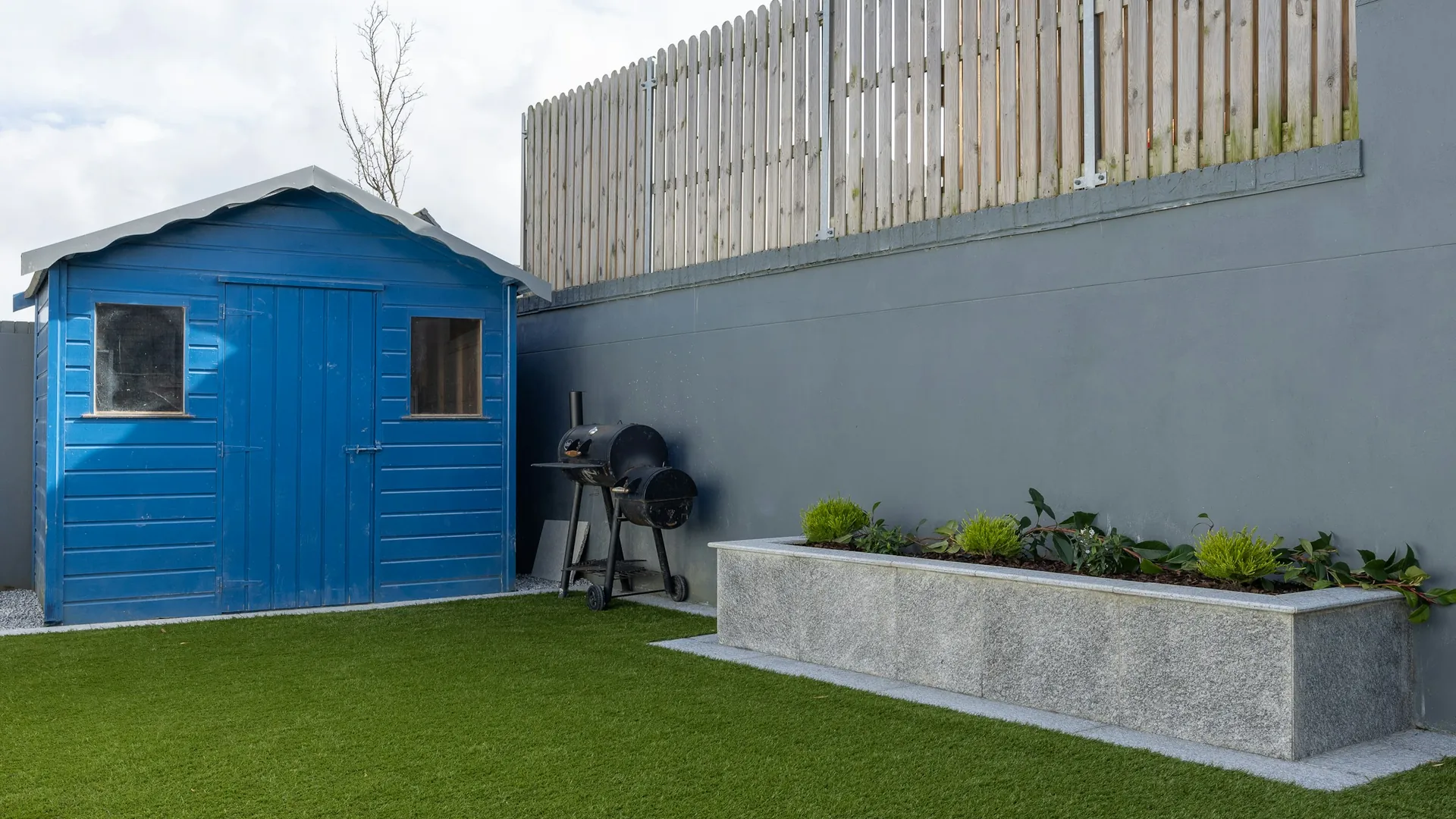 An enclosed back garden laid to artificial grass, with a shed and fencing