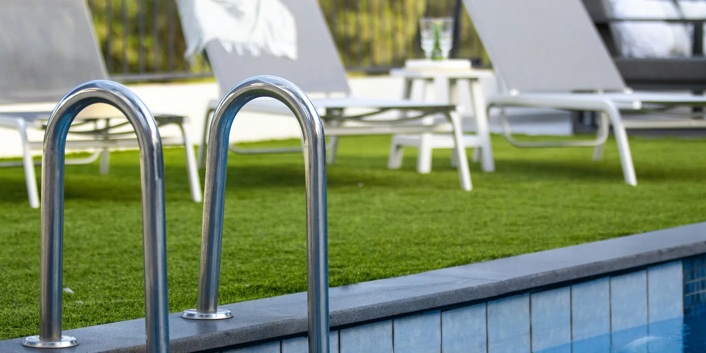 A large artificial lawn laid beside a pool and loungers